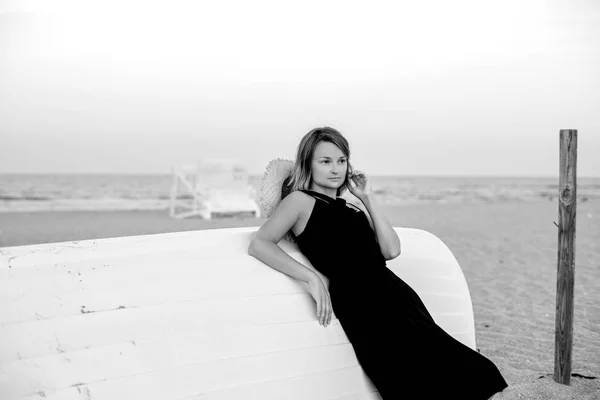 Mulher bonita em vestido de verão preto na praia perto de barco de madeira branca . — Fotografia de Stock