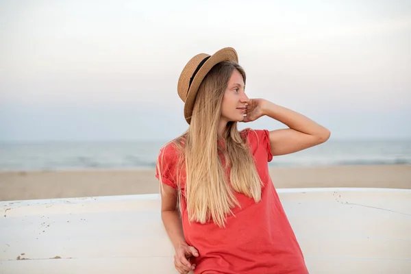 Femeia frumoasă cu păr lung poartă pălărie de paie pe plajă lângă barca de lemn . — Fotografie, imagine de stoc