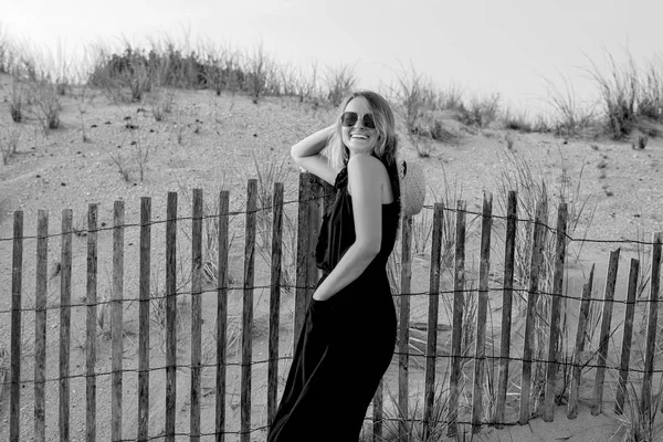 Beautiful woman in black summer dress on the beach near wooden fence. — Stock Photo, Image