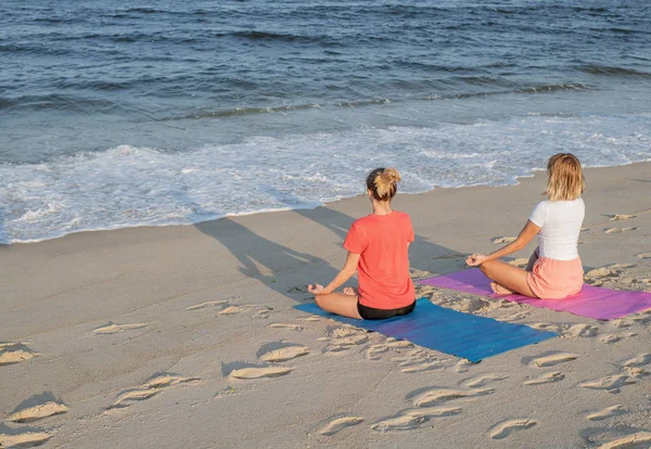 标题： 年轻女性在日落时在海滩上练习瑜伽。女孩冥想，坐在莲花姿势 — 图库照片