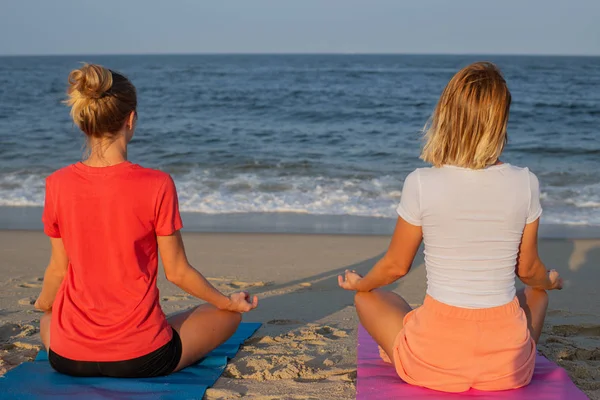 标题： 年轻女性在日落时在海滩上练习瑜伽。女孩冥想，坐在莲花姿势 — 图库照片