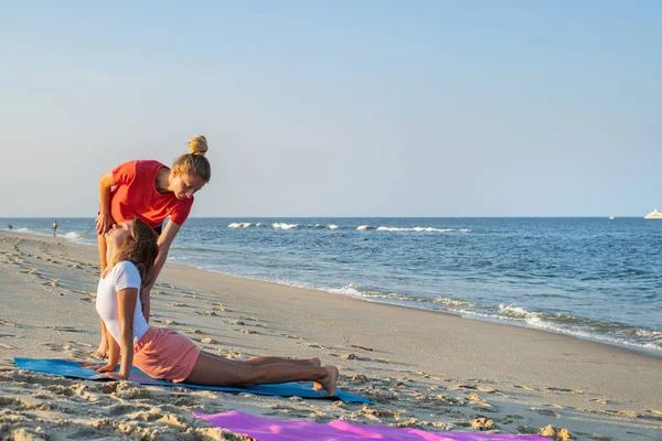 Instructorul de clasă Yoga ajută începătorul să facă exerciții de asana. Femeia care face yoga cu antrenorul pe plajă — Fotografie, imagine de stoc