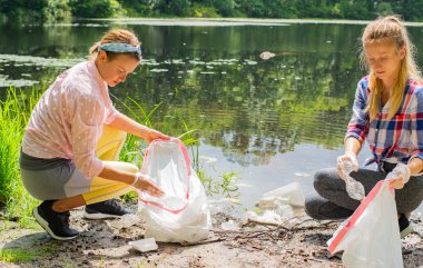 Gönüllüler nehir kenarında çöp leri temizliyorlar. Gölde şişe plastik toplayan kadınlar, kirlilik ve çevre.