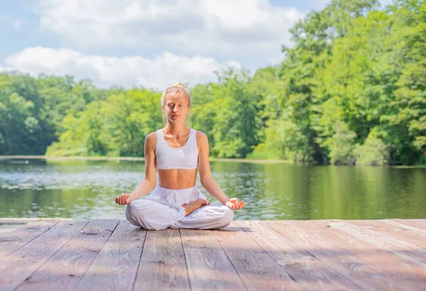 Mujer atractiva está practicando yoga y meditación, sentado en la pose de loto cerca del lago por la mañana . — Foto de Stock