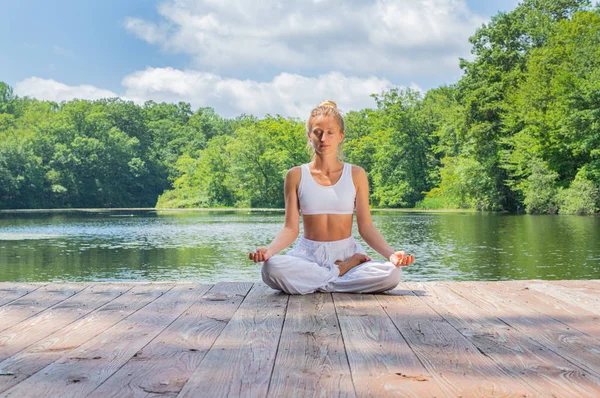 有吸引力的女人正在练习瑜伽和冥想,早上坐在湖边的莲花姿势. — 图库照片