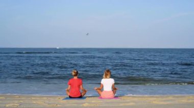 Genç kadınlar güneşin batımında sakin plajda yoga yapıyorlar. Meditasyon kızlar, Lotus oturan deniz kıyısında poz.