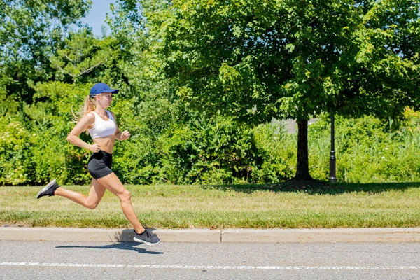 Deportiva mujer en pista de ropa deportiva corriendo en la carretera. Atleta chica es trotar en el parque . — Foto de Stock