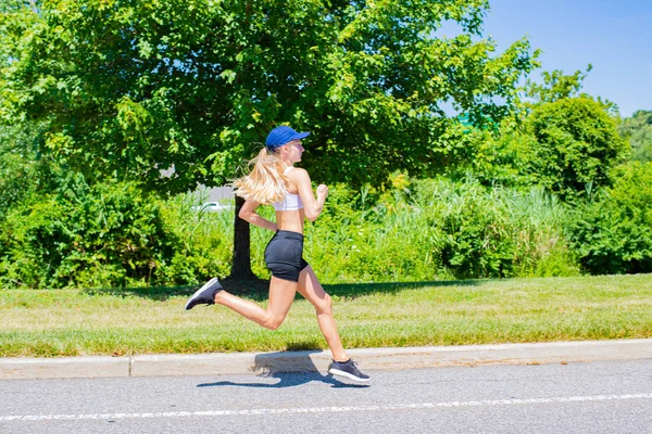 Deportiva mujer en pista de ropa deportiva corriendo en la carretera. Atleta chica es trotar en el parque . — Foto de Stock