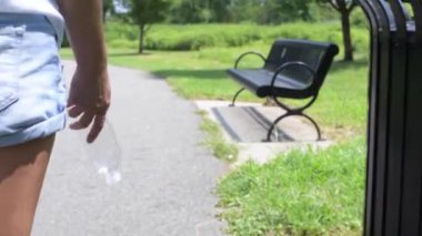 Parkta çimlerin üzerine plastik şişe atan ve giden bir kadın. Çevre kirliliği, insanlar sokağa çöp atıyor.