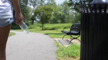 Parkta çimlerin üzerine plastik şişe atan ve giden bir kadın. Çevre kirliliği, insanlar sokağa çöp atıyor.