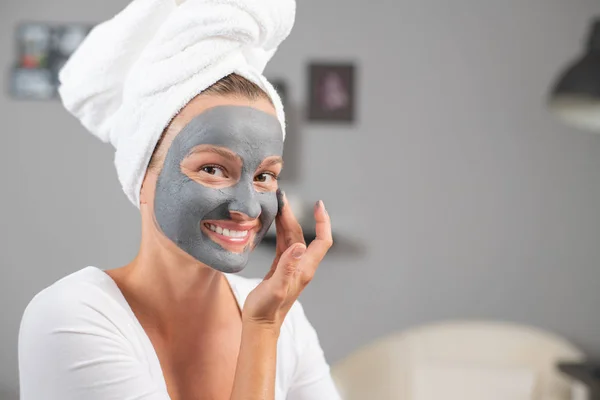 Beautiful woman is applying facial clay mask. Beauty treatments and skincare — Stock Photo, Image