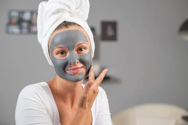 Beautiful woman is applying facial clay mask. Beauty treatments and skincare