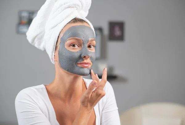 Beautiful woman is applying facial clay mask. Beauty treatments and skincare — Stock Photo, Image