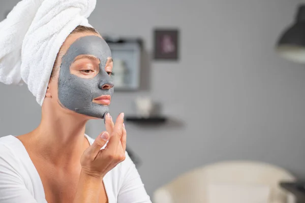 Beautiful woman is applying facial clay mask. Beauty treatments and skincare — Stock Photo, Image