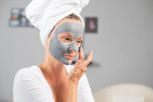 Beautiful woman is applying facial clay mask. Beauty treatments and skincare — Stock Photo, Image