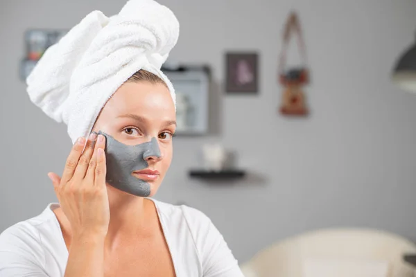 Hermosa mujer está aplicando máscara de arcilla facial. Tratamientos de belleza y cuidado de la piel — Foto de Stock