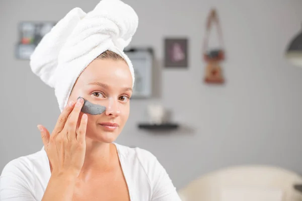 Beautiful woman is applying facial clay mask. Beauty treatments and skincare — Stock Photo, Image