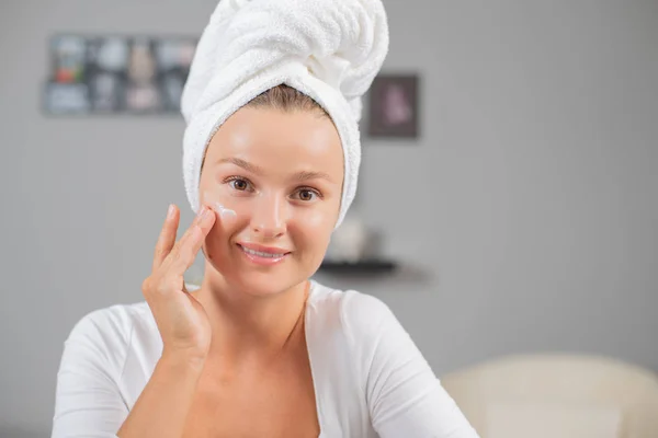 Giovane donna felice che si applica la crema sul viso. Donna viso cura della pelle . — Foto Stock