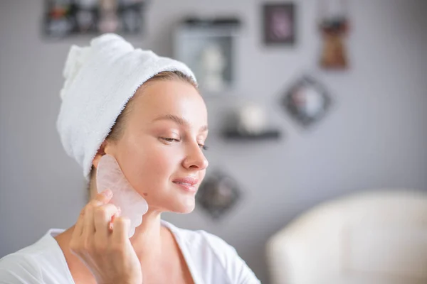 Massagem facial. Mulher bonita está recebendo rosto de massagem usando pedra de jade para cuidados com a pele — Fotografia de Stock