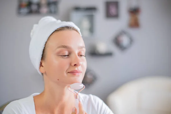Face massage. Beautiful woman is getting massage face using jade facial roller for skin care — Stock Image Face massage. Beautiful woman is getting massage face using jade facial roller for skin care Stock Photo