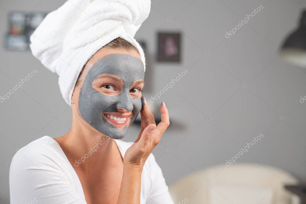 Beautiful woman is applying facial clay mask. Beauty treatments and skincare