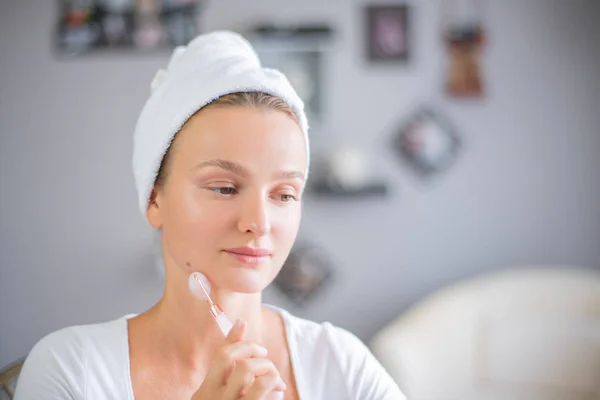 Massage du visage. Belle femme se fait masser le visage en utilisant un rouleau facial en jade pour les soins de la peau — Photo