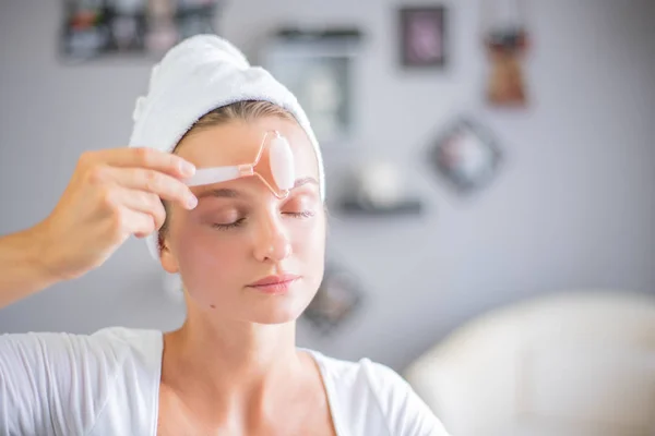 Massagem facial. Mulher bonita está recebendo rosto de massagem usando jade rolo facial para cuidados com a pele — Fotografia de Stock