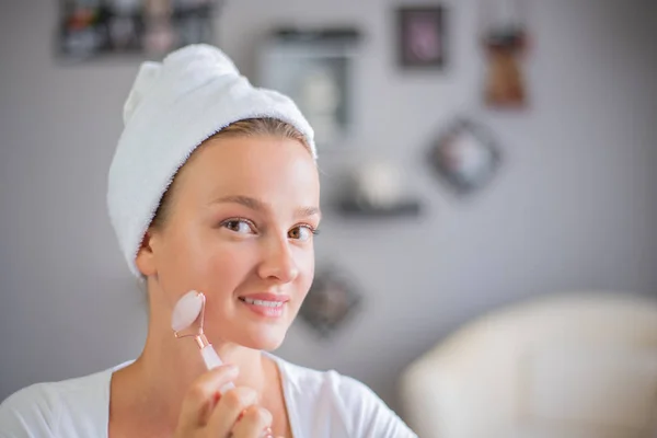 Massagem facial. Mulher bonita está recebendo rosto de massagem usando jade rolo facial para cuidados com a pele — Fotografia de Stock
