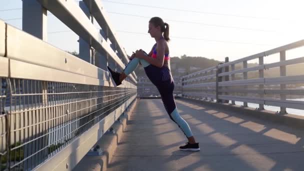 スポーツ女性は走る前に足を伸ばす 桟橋で朝のエクササイズをしている若い女性 — ストック動画