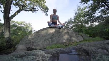 Genç kadın yavaş çekimde bir dağın tepesinde güzel egzotik bir yerde yoga yapıyor. Yoga ve meditasyon.