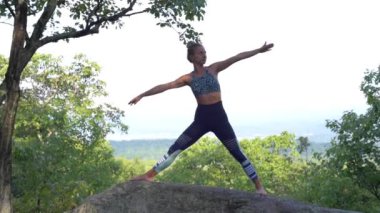 Genç kadın yavaş çekimde bir dağın tepesinde güzel egzotik bir yerde yoga yapıyor. Yoga ve meditasyon.