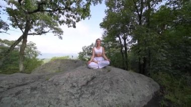 Genç kadın yavaş çekimde bir dağın tepesinde güzel egzotik bir yerde yoga yapıyor. Yoga ve meditasyon.