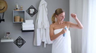 Vücut bakımı. Duştan sonra havluya sarılmış güzel kadın antiperspirant kullanıyor. Kız koltuk altı derisi için deodorant sprey kullanıyor