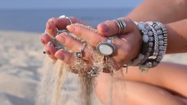 美丽的女人的手手手镯和戒指是倾泻沙通过手指在沙滩上缓慢运动 — 图库视频影像