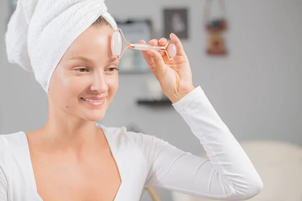Masaje facial. Hermosa mujer está recibiendo cara de masaje utilizando rodillo facial de jade para el cuidado de la piel — Foto de Stock