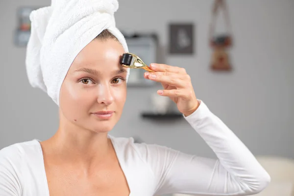 Beautiful woman is using anti aging derma roller. Woman is making needles procedure on face using meso roller. — Stock Photo, Image