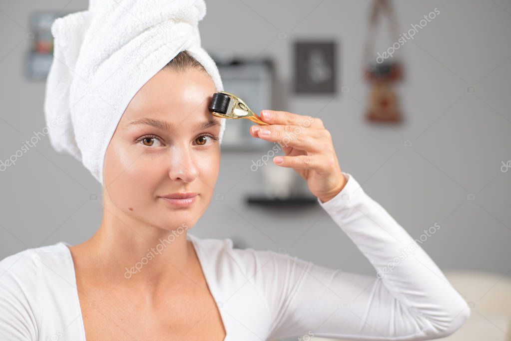 Beautiful woman is using anti aging derma roller. Woman is making needles procedure on face using meso roller.
