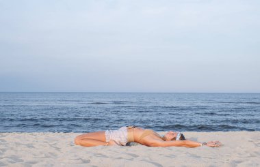 Sahilde yoga yapan genç bir kadın. Supta Virasana