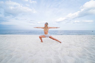 Sahilde yoga yapan genç bir kadın. Savaşçı poz