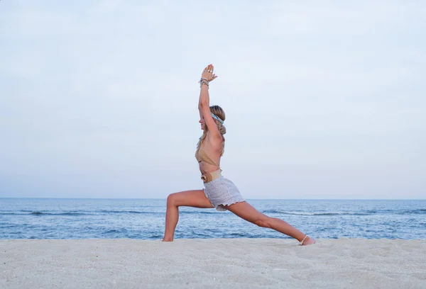 O tânără practică yoga pe plajă. Virabhadrasana pozez — Fotografie, imagine de stoc