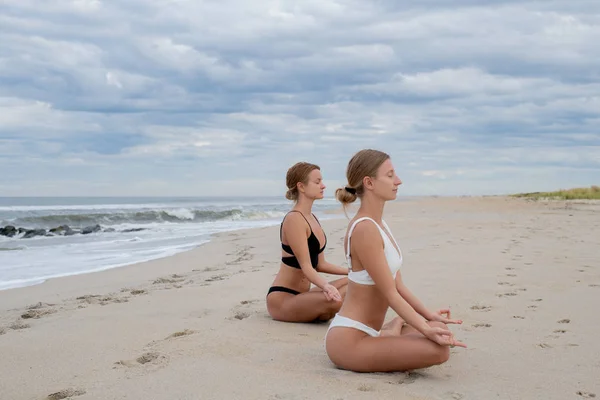 Молодые женщины практикующие йогу в позе лотоса на пляже — стоковое фото