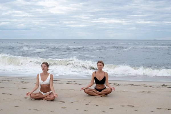 Молодые женщины практикующие йогу в позе лотоса на пляже — стоковое фото