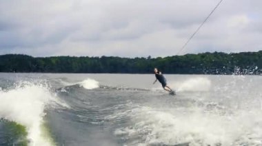 Ekstrem su sporları. Genç adam göldeki wakeboard'da numaralar yapıyor. Wakeboard binici su sıçramaları hızlı hareket