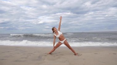 Genç kadın yavaş çekimde sahilde yoga yapıyor. Güzel kız deniz kıyısında yoga yapıyor.