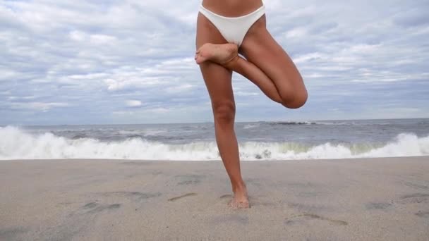 スローモーションでビーチでヨガを練習している若い女性 海岸で木のポーズでヨガをしている美しい女の子 — ストック動画
