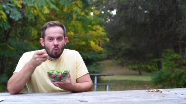 Parkta oturan taze salata yiyen adam. Sağlıklı beslenme, diyet konsepti ve vegan gıda