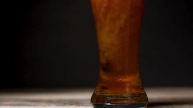 Bira köpüğü kenardan aşağıya yakın çekim yapıyor. Siyah arka planda bir bardak soğuk bira.. 