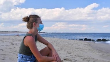 Coronavirus sırasında turizm, plajda oturan maskeli kadın. Coronavirüs salgınından sonraki yaşam. Yeni kurallar ve sosyal uzaklık.