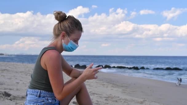 Coronavirus Sırasında Turizm Maskeli Bir Kadın Kumsalda Otururken Akıllı Telefon — Stok video