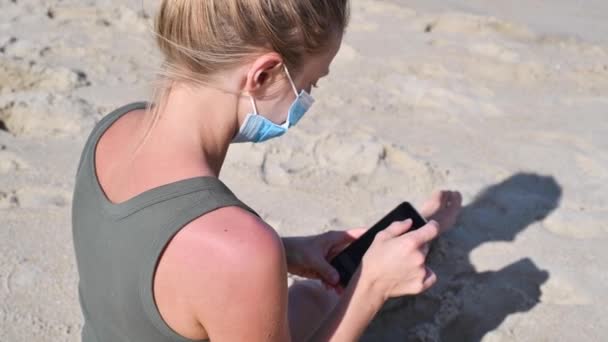 Coronavirus Sırasında Turizm Maskeli Bir Kadın Kumsalda Otururken Akıllı Telefon — Stok video